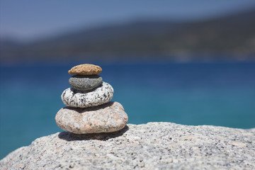 Fototapeta na wymiar Relax Zen stones. Background sea for the perfect meditation. Stones pyramid in the sun, coast in the distance. 