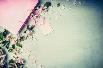 Red and pink shopping bags with summer or spring flowers and leaves on a light mint background, top view, frame Spring or summer sale and shopping concept