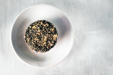 Sweet cupcake sprinkled with nuts on a white plate and a textured wooden table.