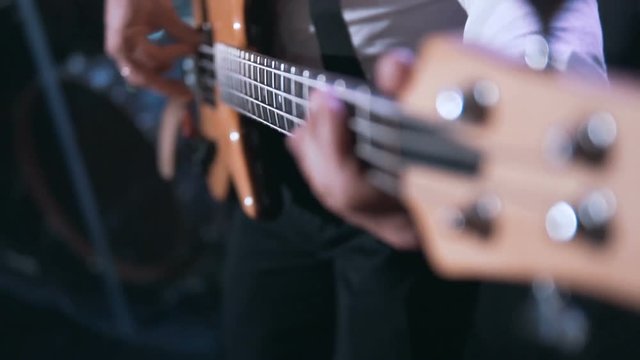 Guitarist wears white shirt playing on bass guitar on the concert stage, 100FPS slowmotion