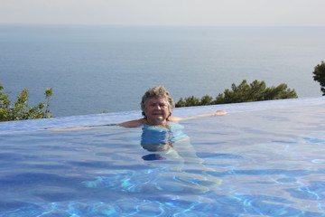A retired lady cooling off in an infinity swimming pool while on vacation, 2017