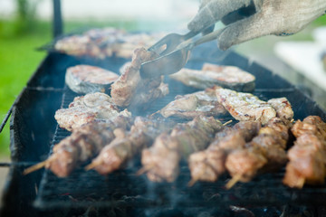 Closeup of a hand moving a piece of meat on a barbecue grill with tongs against a steaming bright background