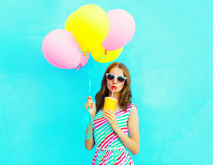 Fashion pretty woman drinks fruit juice from cup holds an air colorful balloons on a blue background