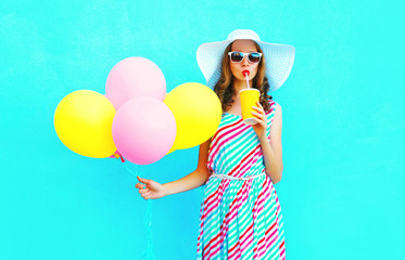 Fashion pretty young woman drinks a fruit juice from cup with an air colorful balloons over a blue background