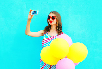 Happy smiling woman taking a picture on a smartphone with an air colorful balloons on a blue background