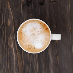 Top view of a white cup of cappuccino on a wooden black table.