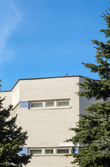 White facade decorated with glossy tiles of a modern building on a background of trees. Bird on the parapet of the building.