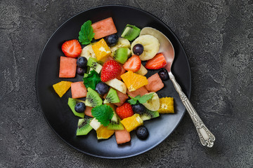 Fresh fruit salad on black plate. Top view