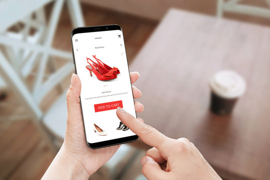 Online store app use on modern mobile phone with round edges. Woman touch add to cart button for red shoes.