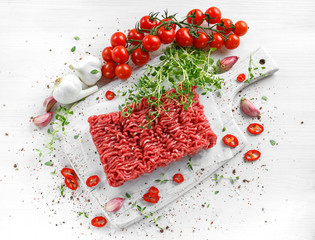 Fresh Raw Beef Minced Meat with salt, pepper, chilli and fresh thyme on white board.