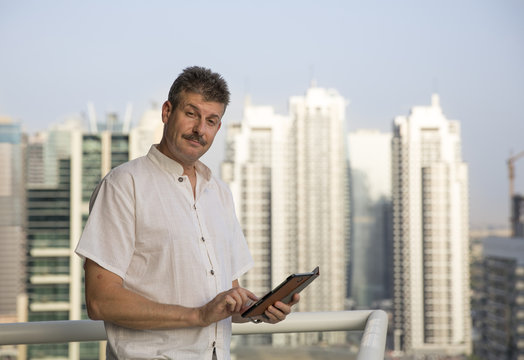 middle aged man at his balcony overlooking the marina, holding a tablet