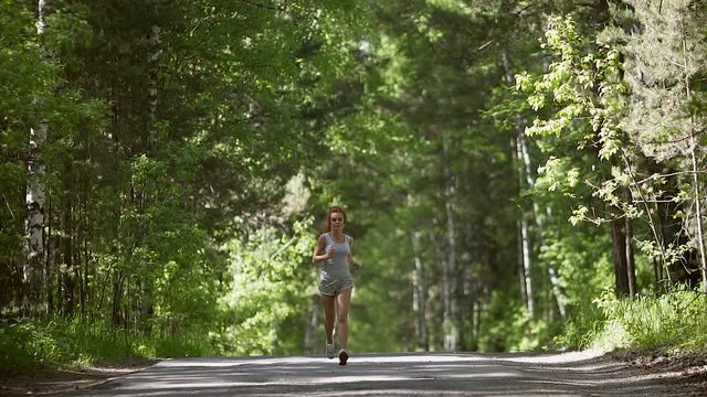 young red-haired girl runs through the forest. Beautiful girl goes in for sports and monitor the health. slow motion