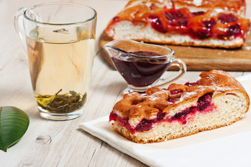 Pie with cherries, cherry jam, tea and white napkin on the table. Dessert, sweet, tea. Green tea. Early morning, breakfast. The background
