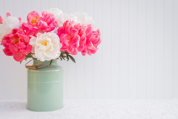 Pink and white peonies in a green vase on a white lace cloth in front of a white beadboard...