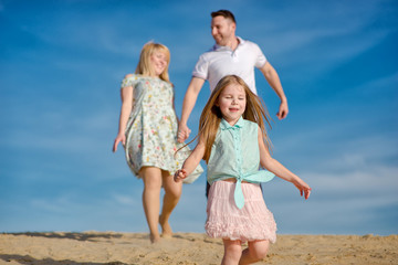 Happy beautiful laughing family running along the sand on the beach against the background blue sky in summer vacation
