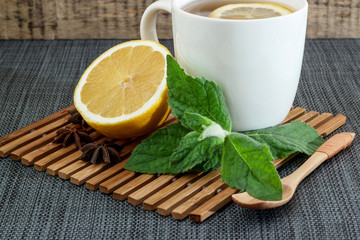 White tea mug with lemon and mint leaves and a wooden spoon