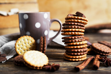Sweets and desserts, chocolate and milk biscuits sandwich, cracker with cinnamon and tea on a dark wooden rustic background 