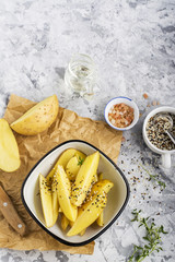 Slices of raw potatoes in seeds of dark and white sesame seeds in a white enamel bowl before baking in the oven. Top view on a marble gray background