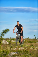 Attractive sportsman riding bike on rocky trail against sky with clouds.