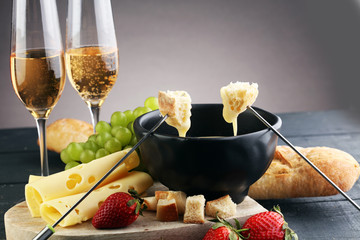 Gourmet Swiss fondue dinner with assorted cheeses on a board and strawberries alongside a heated...
