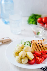 Useful, hearty and delicious breakfast or dinner, boiled potato with dill, cherry tomato, cucumber, white bread toast, vegetable or olive oil and mineral sparkling water on a light wooden background
