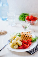Useful, hearty and delicious breakfast or dinner, boiled potato with dill, cherry tomato, cucumber, white bread toast, vegetable or olive oil and mineral sparkling water on a light wooden background