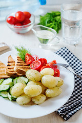 Useful, hearty and delicious breakfast or dinner, boiled potato with dill, cherry tomato, cucumber, white bread toast, vegetable or olive oil and mineral sparkling water on a light wooden background