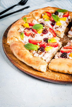 Summer snacks. Food for party. Fruit pizza with cream, currants, yogurt, strawberries, mango, peaches, bananas, blackberries, chocolate, walnuts, mint. On light blue table. Copy space