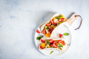 Summer snacks. Food for a party. Fruit tacos with strawberries, mangoes, bananas, chocolate, mint. On a light blue concrete table. Copy space top view