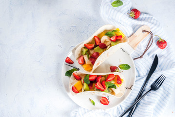 Summer snacks. Food for a party. Fruit tacos with strawberries, mangoes, bananas, chocolate, mint. On a light blue concrete table. Copy space