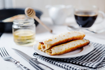 Traditional breakfast or lunch, in a hotel or restaurant, thin pancakes with cottage cheese, honey, coffee and milk on a white wooden background 