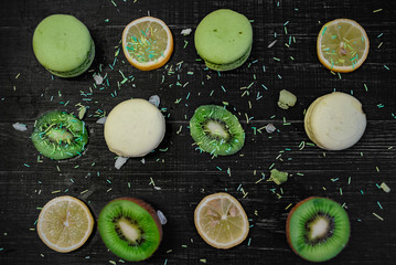 Green and white macaroons with kiwi, orange and lemon in order on a wood gark table