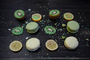 Obraz na płótnie Canvas Green and white macaroons with kiwi, orange and lemon in order on a wood gark table