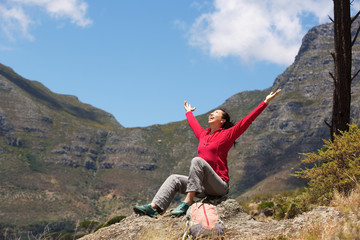 asian female hiker sitting on the peak with arms raised to the sky