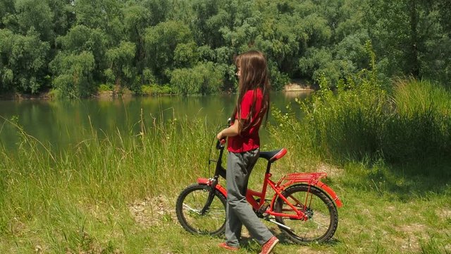 Child with a bicycle in nature. Little girl on a red bicycle by the river.