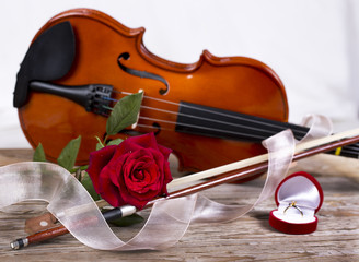 Fototapeta premium Marriage proposal with gold ring, red rose and violin on wooden table