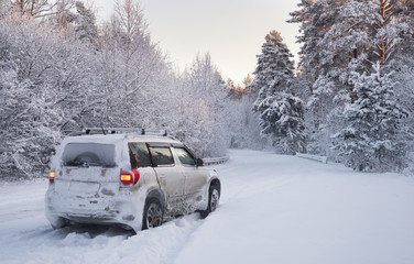 Off-Road Winter Adventure, White SUV Car On Road With Much Snow In Winter Pine Forest. White Crossover Covered With Snow On The Road Among The Winter Forest.
Car And Falling Snow In Winter 
