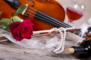 Violin, red rose, pearl necklace and wine on wooden table 