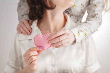 mother's hands and a child's hand holding a red heart together
