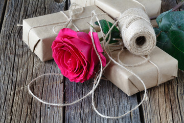 One red rose and gift box with ribbon on rustic wooden table with copy space.