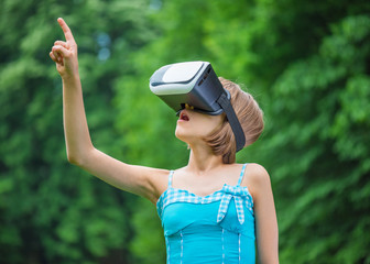 Playful little girl using virtual reality goggles outdoor in summer park. Kid looking in VR glasses. Child have fun experiencing 3D gadget technology.