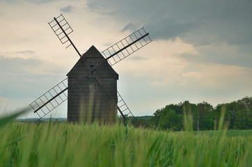 Old wooden wind mill with green field and cloudy sky