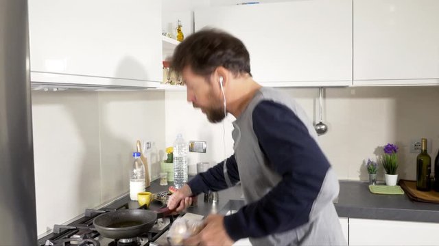 Happy man in kitchen in the morning cooking eggs while dancing listening music