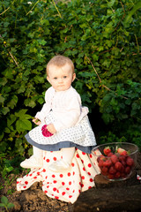 Girl 8 months old European Ukrainian little baby on a walk in the garden holds a flower and strawberries in her hands