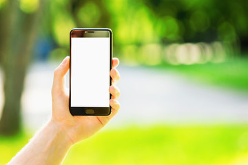 Mockup of male hand holding cellphone with blank screen at green outdoors background.