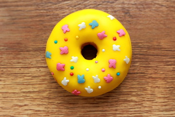 Single yellow donut on a wood background. Rainbow dots decoration. Lemon, melon, pineapple, mango, banana flavour