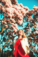 Beautiful happy young woman enjoying warm sunny day in spring garden, wearing bright red dress, eyes closed