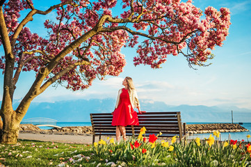 Young blond woman admiring amazing view of Lake Geneva, Switzerland. Woman sitting on the bench under blossom magnolia tree © annanahabed