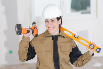 female builder with spirit level and electric drill