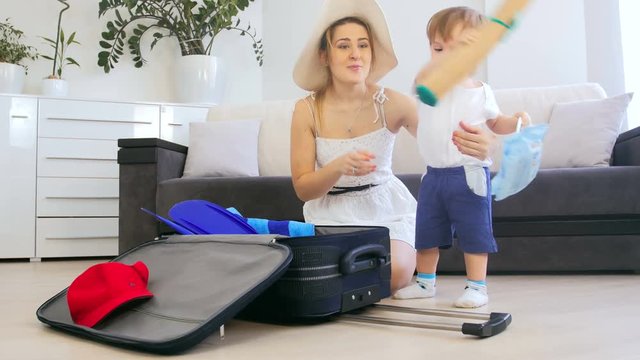 4k video of adorable toddler boy helping mother packing things in suitcase